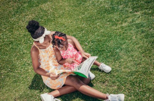 mom and child enjoying the sunshine, reading a book together in the grass