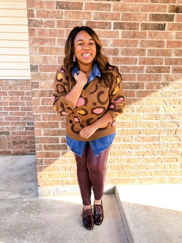 smiling african american woman wearing dark burgundy leather leggings and a v-neck sweater layered over a denim button down