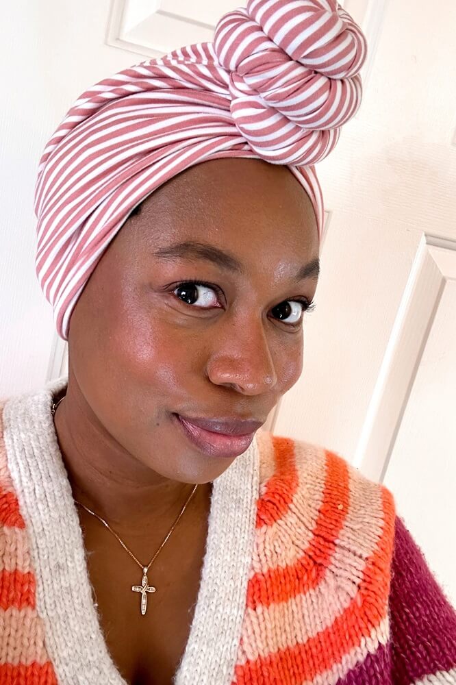 smiling black woman wearing a pink striped turban style headwrap