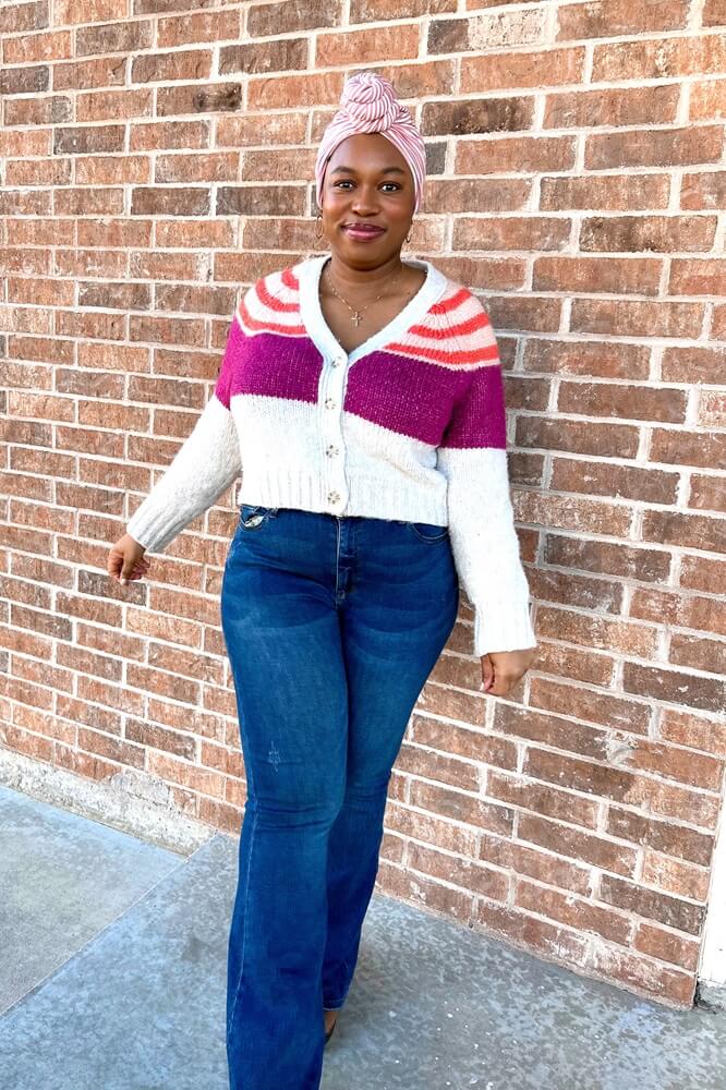 black woman wearing a colorful sweater, jeans, and a striped pre-tied headwrap