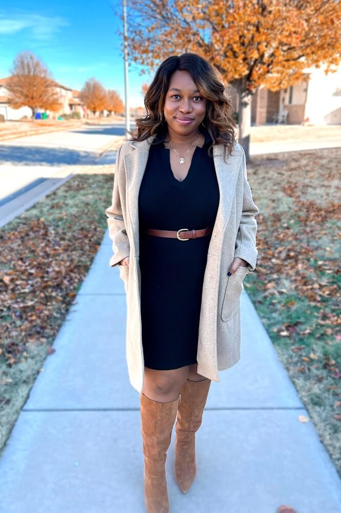 african american woman wearing a black dress, light tan coat, and brown knee high boots
