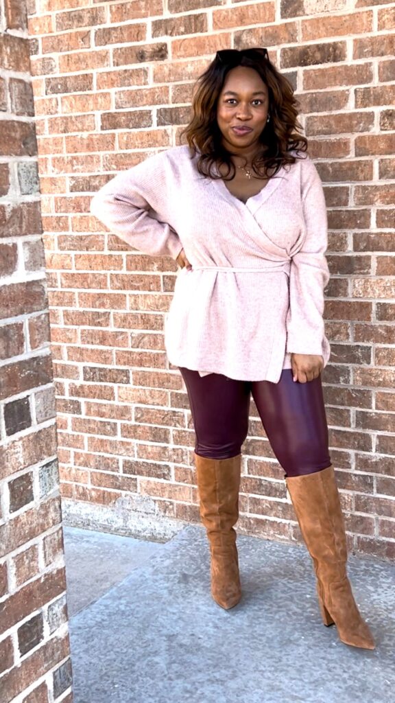smiling black woman wearing a light pink sweater, burgundy leather leggings, and brown suede knee high boots