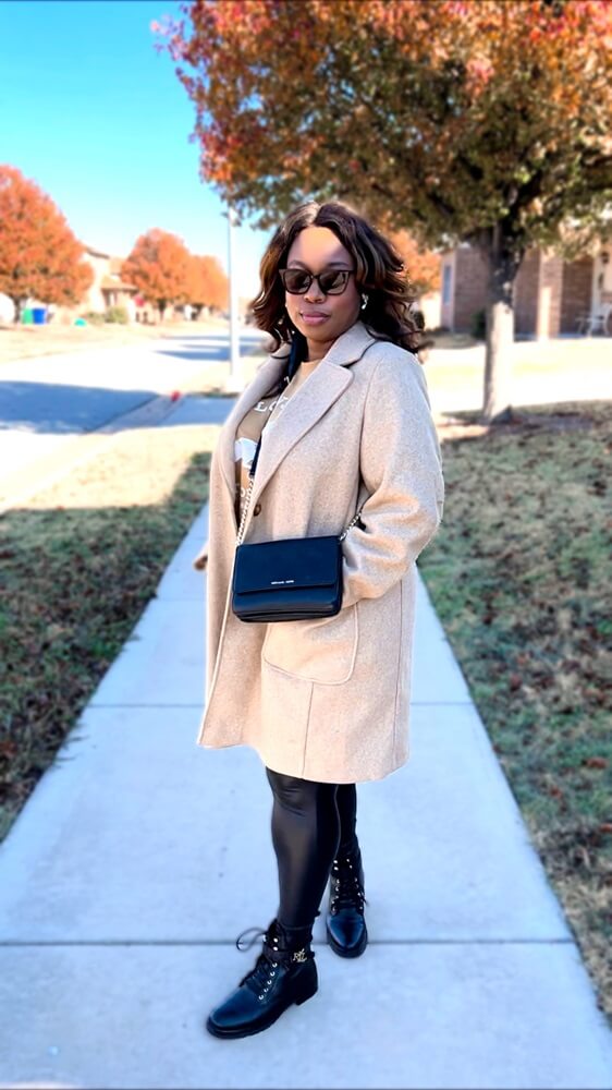 cute stay at home mom outfit idea: black woman wearing a tan overcoat, black leather leather leggings, and combat boots with a black crossbody bag